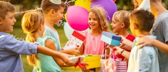 Kinder feiern Geburtstag im Garten mit bunten Luftballons und Geschenken, lachen und freuen sich zusammen.