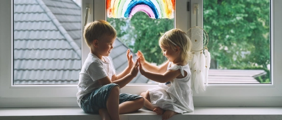 Zwei Kleinkinder sitzen auf der Fensterbank und klatschen sich in die Hände.