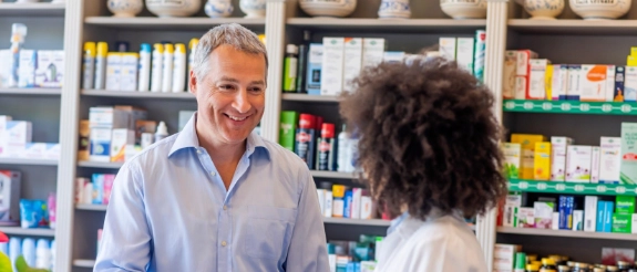 Apotheker berät Kundin an der Kasse einer Apotheke, Regale mit Medikamenten im Hintergrund