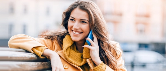 Lächelnde Frau in gelbem Pullover telefoniert mit blauem Smartphone