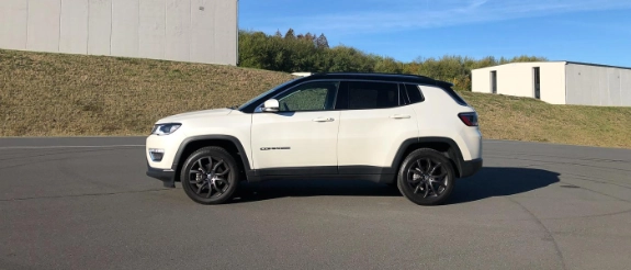 Weißes SUV mit schwarzem Dach parkt auf Asphaltfläche vor Industriegebäuden bei Tageslicht