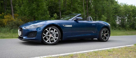 Blauer offener Sportwagen auf Landstraße mit Bäumen im Hintergrund, sonniger Tag