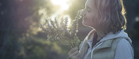 Frau riecht an Lavendelblüten in sonniger Gartenumgebung, warmes Licht im Hintergrund