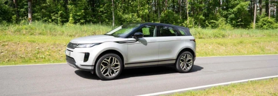 Weißer Range Rover Evoque auf Asphaltstraße vor Waldkulisse, Seitenansicht