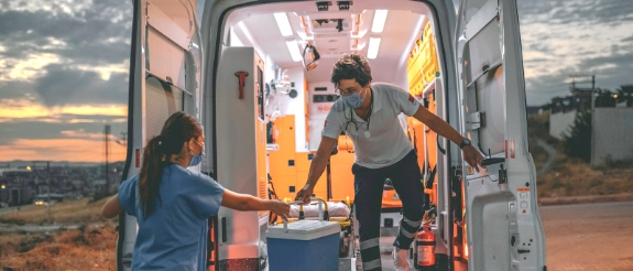 Geöffnete Transporterklappe mit mehreren Personen im Inneren, Sonnenuntergang über ländlicher Landschaft im Hintergrund.