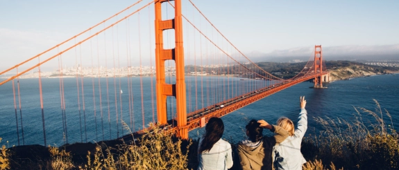 3 junge Leute genießen die Aussicht auf die Golden Gate Bridge bei Ihrem Urlaub in den USA.