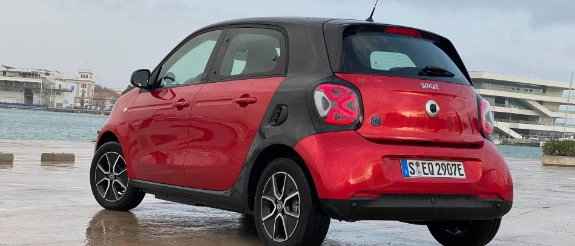 Roter Renault Twingo hintere Ansicht auf Parkplatz mit Stadtkulisse im Hintergrund