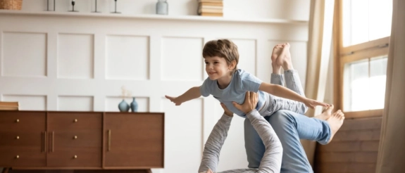 Vater liegt auf dem Rücken und hebt seinen Sohn spielerisch in die Luft im hellen Wohnzimmer