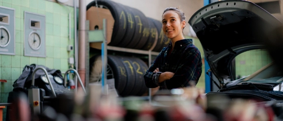 Eine junge Frau steht in einer Autowerkstatt vor einem Regal mit Autoreifen.