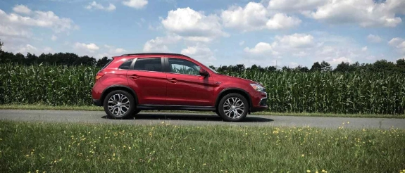 Roter SUV steht auf grüner Wiese mit Blumenfeld, bewölkter Himmel, Waldrand im Hintergrund
