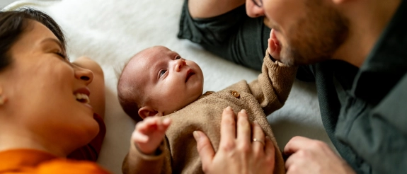 Eltern halten ihr Neugeborenes in den Armen und betrachten es liebevoll, Familie im Schlafzimmer
