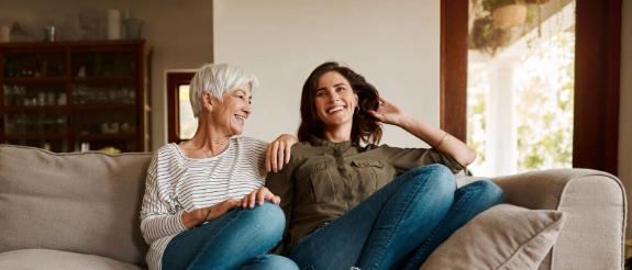 Eine Oma umgeben von ihrer Enkelin auf der Couch sprechen über das Sparen für Kinder