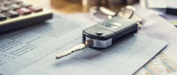 Autoschlüssel auf Schreibtisch neben Taschenrechner, Notizbuch und verschwommenem Auto im Hintergrund