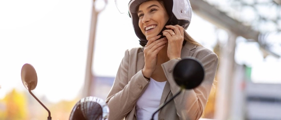 Eine Mopedfahrerin zieht sich einen Helm an als Symbol für eine guten Versicherungsschutz. 