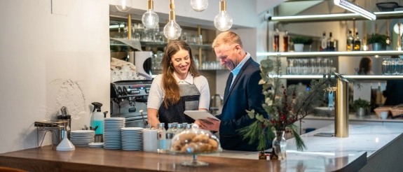 Barista und Kunde an Kaffeetheke mit hängenden Leuchten und modernem Café-Interior