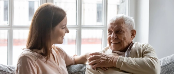 Pflegekraft sitzt nah an Senior und berührt ihn liebevoll an Schulter