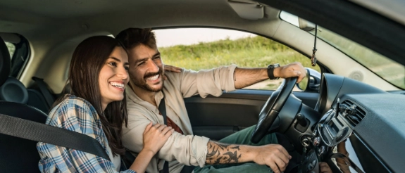 Ein Mann und eine Frau fahren im Auto. Sie lachen und sie berührt ihn am Arm.
