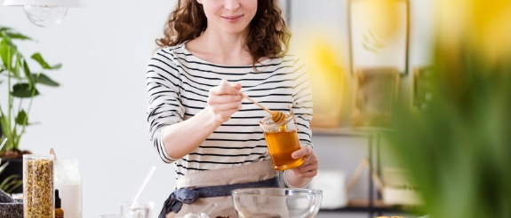 Frau in gestreiftem Shirt hält Glas mit Orangensaft in moderner Küche mit Pflanzen und Lebensmitteln