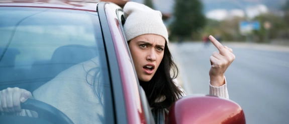 Frau macht rüde Geste im Auto.