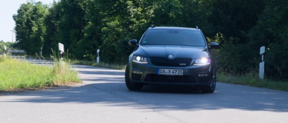 Schwarzer BMW fährt auf Landstraße mit Bäumen und grünen Wiesen an sonnigem Tag