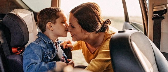 Mutter küsst ihren kleinen Sohn zärtlich auf die Stirn, beide lächeln, warmes Sonnenlicht im Hintergrund