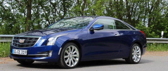 Blauer Cadillac CTS Coupé auf Parkplatz mit grünen Bäumen im Hintergrund