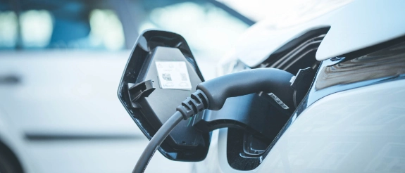 Ladekabel in Ladestation eines Elektrofahrzeugs, unscharfes Auto im Hintergrund