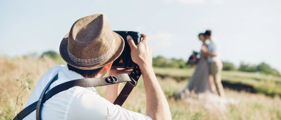 Mann mit Strohhut fotografiert Frau in Kleid auf ländlichem Feld mit Kamera