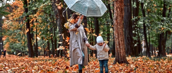 Zwei Kinder mit transparentem Regenschirm in herbstlichem Wald mit buntem Laub am Boden
