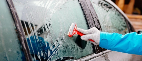 Person enteist Autoscheibe mit Eiskratzer.