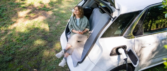 Eine Frau lädt ihr Elektroauto während sie im Kofferraum sitzt und wartet.