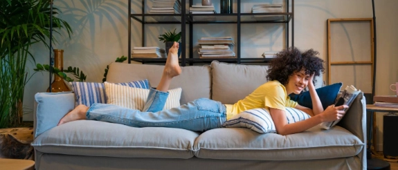 Eine Frau liegt auf ihrem Sofa und liest eine Zeitschrift.