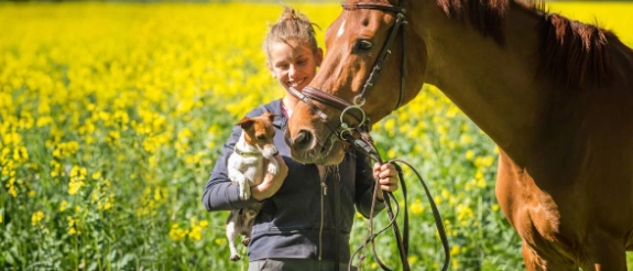 Eine Frau mit einem Hund auf dem Arm und einem Pferd.