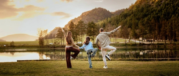 Familie macht Yoga im Freien, Mutter und Vater und Kind halten sich an den Händen.