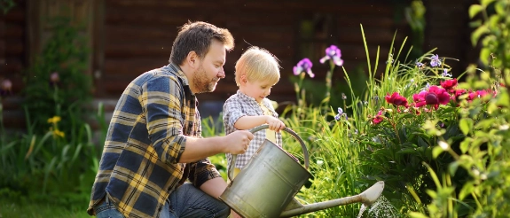 Vater gießt mit seinem Sohn Blumen in einem Garten für Kinder.