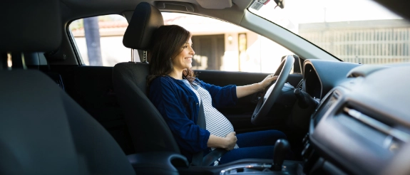 Eine werdende Mutter sitzt mit Babybauch am Steuer als Symbol für das Autofahren in der Schwangerschaft.