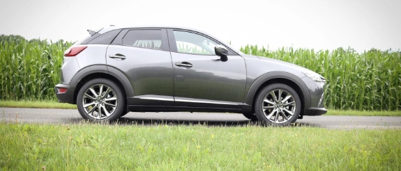 Grauer SUV von der Seite auf Landstraße mit Grünflächen und bewölktem Himmel
