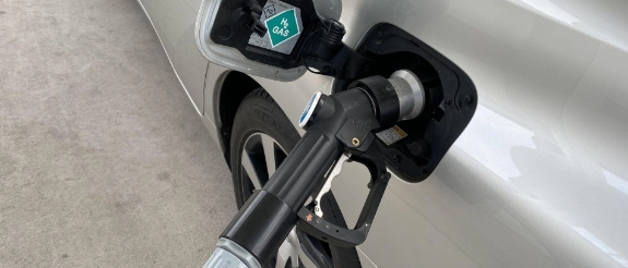 Elektroauto-Ladestecker an Ladesäule mit leuchtender grüner Anzeige, Hand hält Stecker, Betonuntergrund