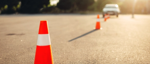 Rote Verkehrskegel auf Asphaltstraße mit Auto und Sonnenuntergang im Hintergrund bei Fahrprüfung