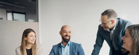 Vier Kolleginnen und Kollegen unterhalten sich in einem Büro vor einem Notebook.