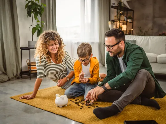 Familie sitzt auf dem Wohnzimmer-Teppich und zählt Geld. Sie freuen sich über die Riester-Zulage. 