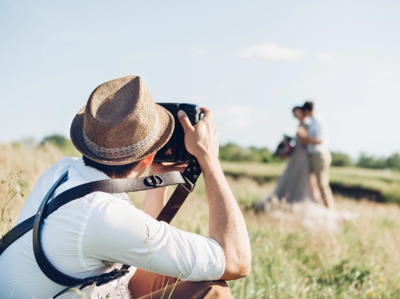 Mann mit Strohhut fotografiert Frau in Kleid auf ländlichem Feld mit Kamera