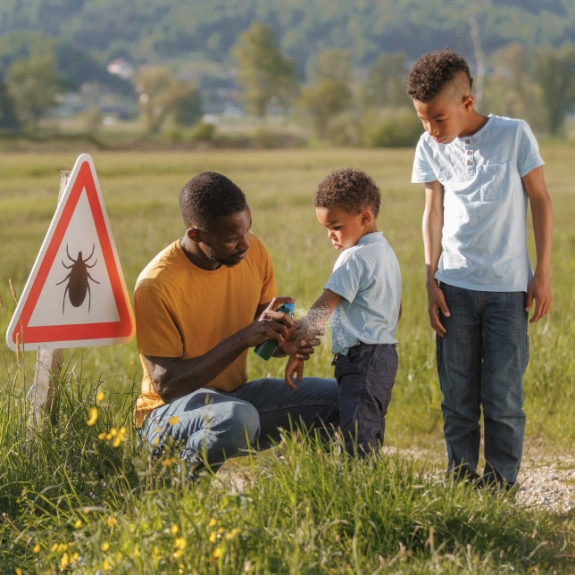 Ein Vater ist meinen Söhnen unterwegs und schützt sie mit Insektenspray vor Zecken.