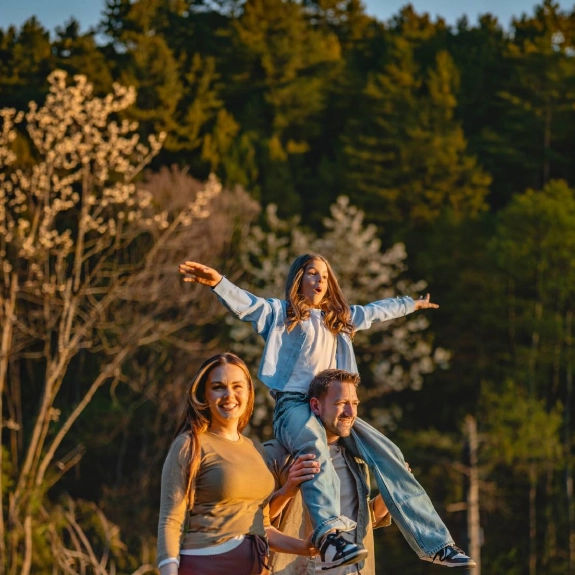 Familie wandert durch den Wald, der Vater trägt die Tochter auf den Schultern.