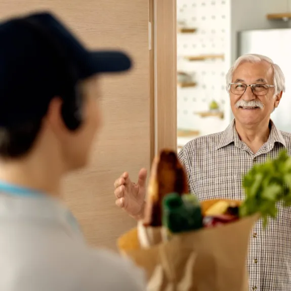 Ein junger Mann liefert einem aelteren Herrn in einer Papiertuete Lebensmittel