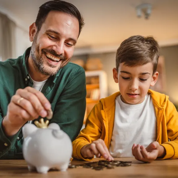 Mit Hilfe der Taschengeldtabelle zählen Vater und Sohn das empfohlene Taschengeld aus einer Spardose.