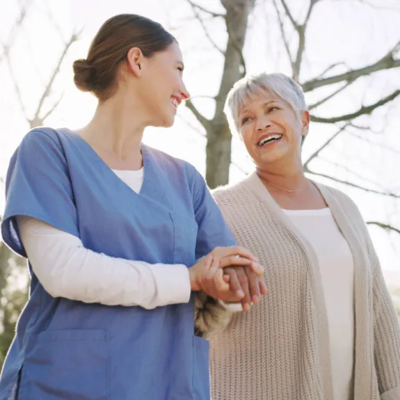 Eine junge Pflegerin hält die Hand einer älteren Dame die lächelt.