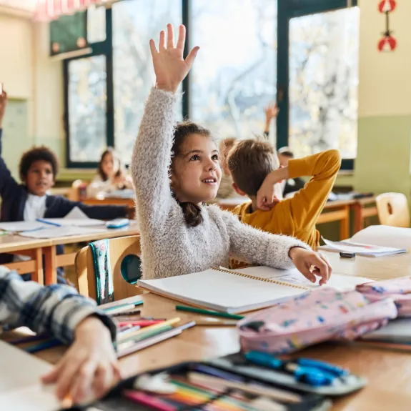 Schüler sitzen an ihren Tischen in der Schulklasse und melden sich eifrig im Unterricht.