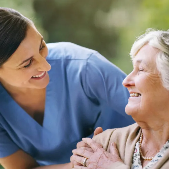 Pflegerin lächelt eine alte Dame an die sie zurück anlächelt.