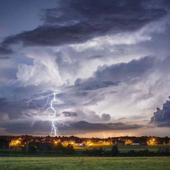 Ein Gewitter mit Blitzen über einer Ortschaft.